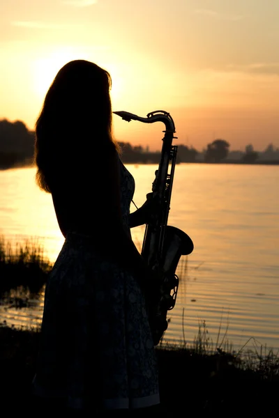 Silhouette eines Mädchens in einem Kleid mit einem Blasinstrument in den Händen, das nachdenklich in die Ferne blickt — Stockfoto