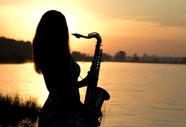 Weibliche Silhouette gegen die Morgendämmerung mit einem Saxophon in der Hand — Stockfoto