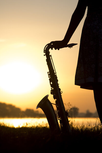 силуэт женщины в платье на фоне красивого заката солнца и небесного саксофона на траве и наслаждаться видом
