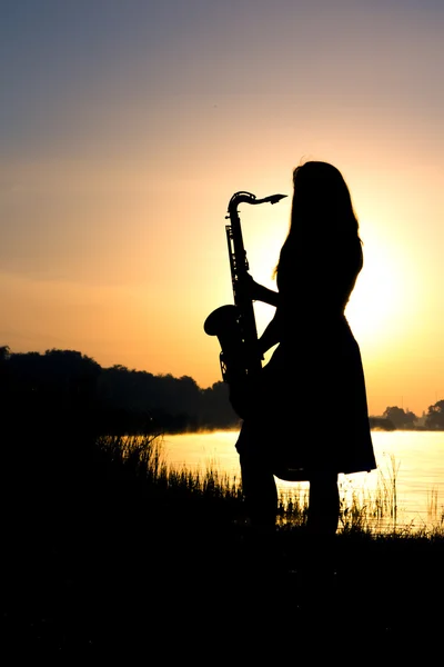 Silhouette eines Mädchens in einem Kleid mit einem Blasinstrument in den Händen, das nachdenklich in die Ferne blickt — Stockfoto