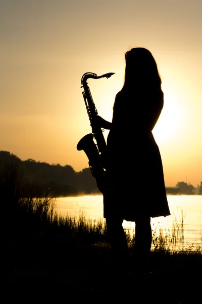 Kvinnliga siluett mot gryningen med en saxofon i hans händer — Stockfoto