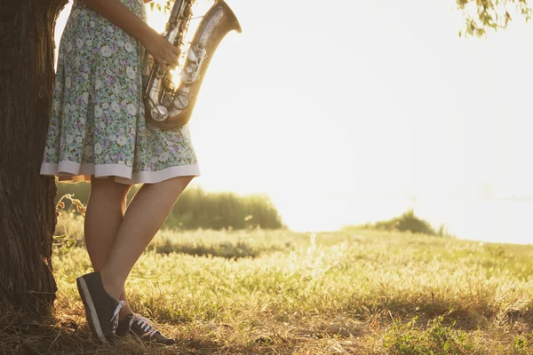 Mujer joven en un vestido se para cerca del árbol en la hierba verde con un instrumento musical de viento en las manos del amanecer — Foto de Stock
