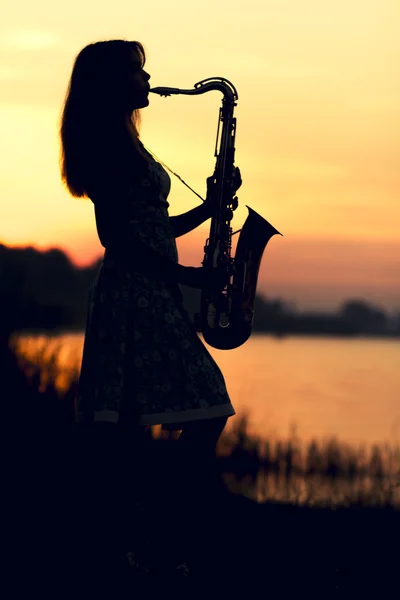 Silhouette eines Mädchens in einem Kleid mit einem Blasinstrument in den Händen, das nachdenklich in die Ferne blickt — Stockfoto