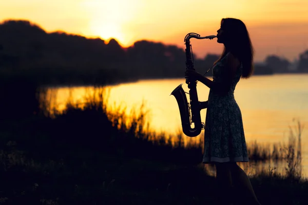 Silhouettenporträt einer Frau in einem Kleid, deren Steckenpferd Musik ist, spielt sie am Flussufer und ruht emotional — Stockfoto