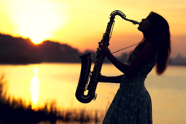 The silhouette portrait of a young woman who skillfully playing the saxophone in the nature that gives her peace of tranquility — Stock Photo, Image