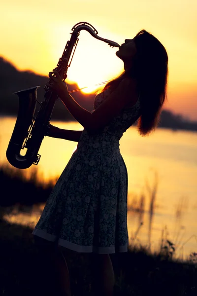Ritratto di una donna in abito che suona il sassofono vicino al fiume — Foto Stock