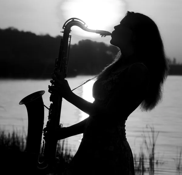 Черно-белый портрет красивой девушки, играющей на саксофоне на озере — стоковое фото