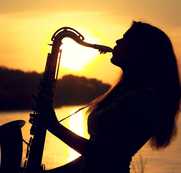 Das Scherenschnitt-Porträt einer jungen Frau, die gekonnt Saxofon spielt in der Natur, die ihr Ruhe verleiht — Stockfoto