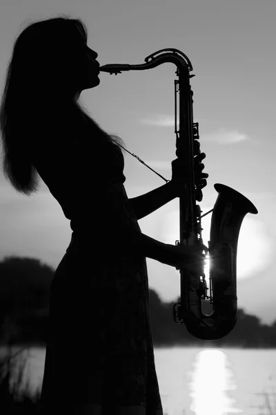 Черно-белый портрет красивой девушки, играющей на саксофоне на озере — стоковое фото