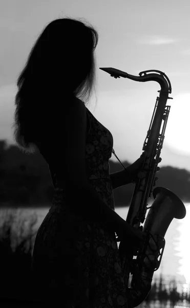 Silueta en blanco y negro de una chica en un vestido con un instrumento musical de latón en sus manos mirando pensativamente a la distancia —  Fotos de Stock