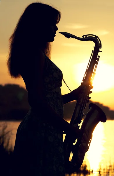Silueta de una chica en un vestido con un instrumento musical de latón en sus manos mirando pensativamente a la distancia — Foto de Stock