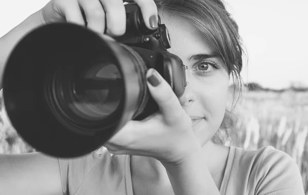 Черно-белое фото девушки, смотрящей в видоискатель камеры в камеру, направленную на природу — стоковое фото