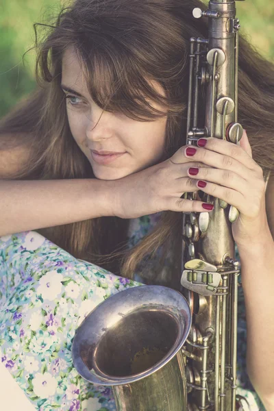 Vintage portrait of half face of a young woman with wind musical instrument in the hand on the lawn