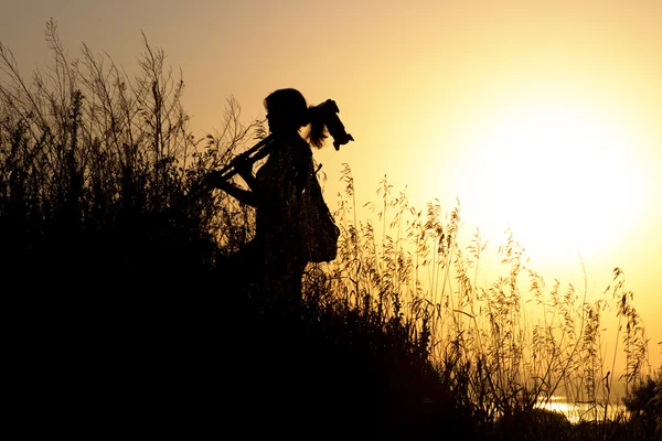 Silhueta de uma jovem mulher viajando no ombro jogando no tripé fotográfico profissional — Fotografia de Stock