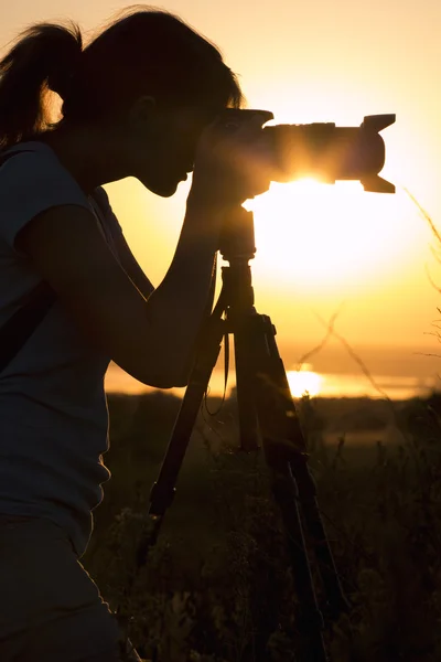 Retrato de silueta de una joven en un campo con una cámara profesional, lente y trípode — Foto de Stock