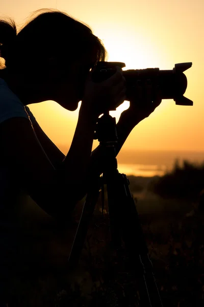 Silhouette porträtt av en ung kvinna i ett fält med en professionell kamera, objektiv och stativ — Stockfoto
