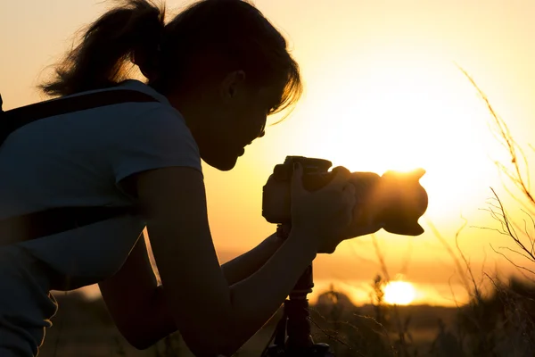 Retrato de silueta de una mujer joven fotografiando una hermosa naturaleza al atardecer en equipo fotográfico — Foto de Stock