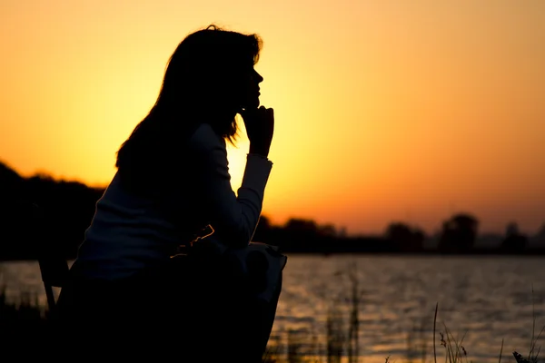 Silhouette portrait d'une belle jeune femme assise sur une chaise au bord de la rivière à l'aube — Photo
