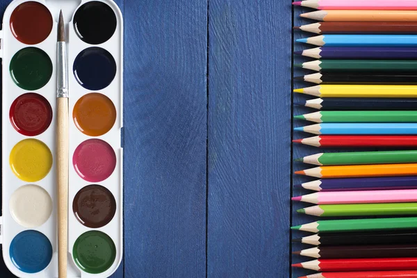 Photo de peintures à l'aquarelle avec un pinceau à peindre et couché devant des crayons de couleur sur le bureau de l'école avec un espace vide pour votre test — Photo