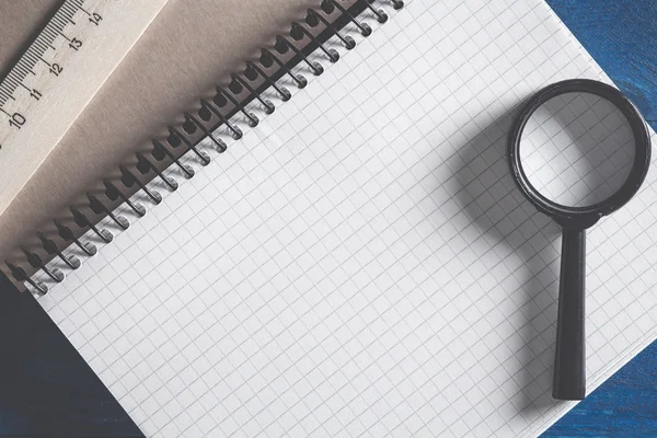 Photo de cahier à spirale dans la cellule couchée sur la table avec une loupe et une règle en bois — Photo