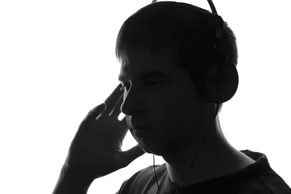 Portrait of the silhouette of a young man who enjoys listening to music on headphones — Stock Photo, Image