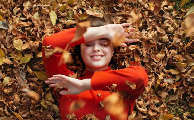 Düşmüş altın sonbahar yapraklarının üzerinde yatan kadın arka plan, açık hava portresi, üst manzara, oynayan mutlu kız