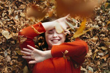 Düşmüş altın sonbahar yapraklarının üzerinde yatan kadın arka plan, açık hava portresi, üst manzara, oynayan mutlu kız