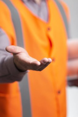 Gri arka planda inşaat projesini yürüten yelek giymiş bir müteahhit, avuç içini gösteren bir mühendis.