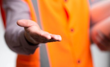 Gri arka planda inşaat projesini yürüten yelek giymiş bir müteahhit, avuç içini gösteren bir mühendis.