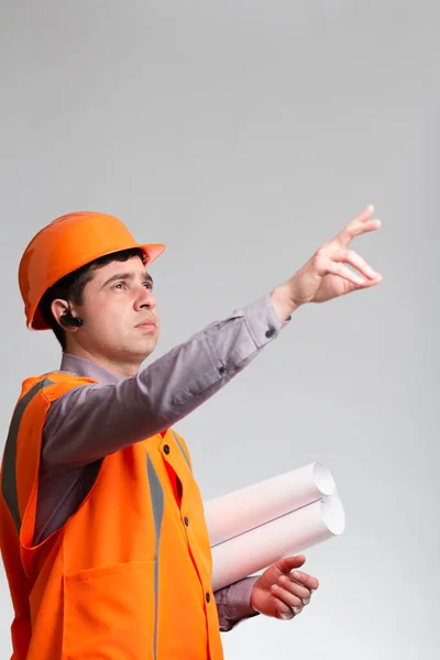 young construction worker in hard hat and reflective vest on grey studio background showing with finger direction forward, manager responsibility