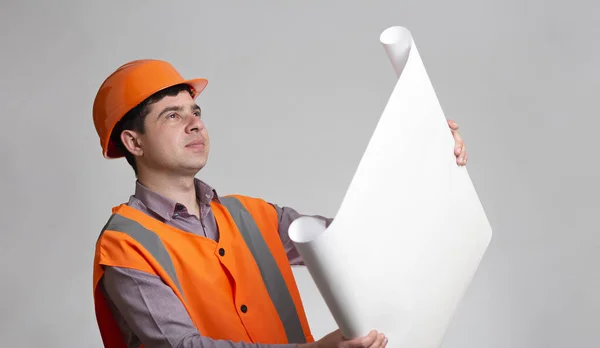 满意的年轻建筑工人 头戴硬帽 手握灰色工作室背景的打开的纸项目 工程师的责任 — 图库照片
