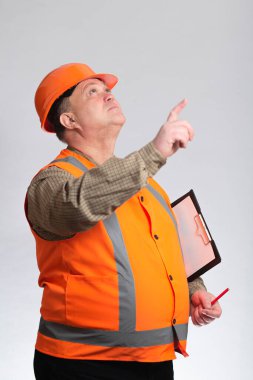 Gri arka planda, kasketli orta yaşlı bir mühendis ve kolunun altında, yukarı bakıyor ve yönetiyor.