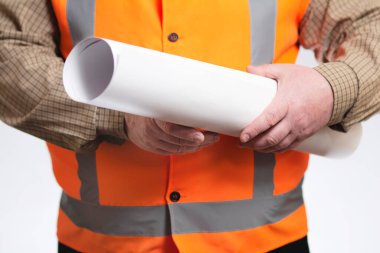 Göbeği gri stüdyo arka planında olan, yansıtıcı yelek giyen şişman inşaat işçisi, kağıt planlı mühendis.