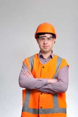 Gri stüdyo arka planında sert şapka ve yansıtıcı yelek giymiş gülümseyen genç inşaat işçisinin portresi, başarılı mühendis.