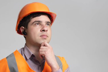 Sert şapkalı ve yansıtıcı yelek giyen genç işadamı gri stüdyo arka planında el ele düşünüyor, endüstri konseptini inşa ediyor.