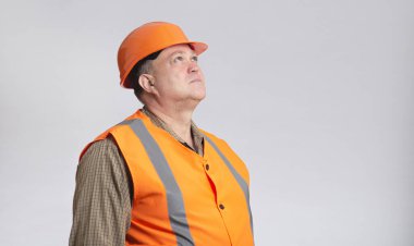 Gri stüdyo geçmişi ve inşaat endüstrisi konsepti üzerine yansıtıcı yelek giymiş orta yaşlı bir inşaat müteahhidinin portresi.