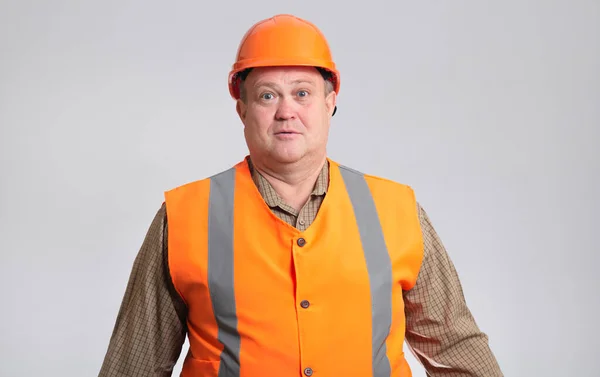 胖胖的建筑工人 头戴硬礼帽 身穿反光背心 滑稽地混淆不清 鬼鬼祟祟地表现出滑稽的表情 — 图库照片
