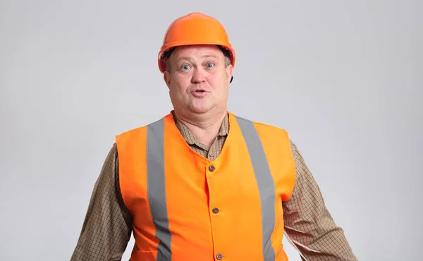 胖胖的建筑工人头戴安全帽 身穿灰色背景的反光背心 滑稽地混淆不清 不懂幽默的表情 — 图库照片