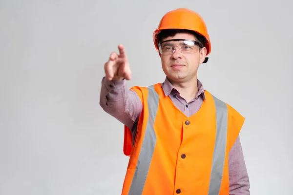 ハードハットの若い建設労働者保護眼鏡と指の方向を示す灰色のスタジオの背景の全体 — ストック写真