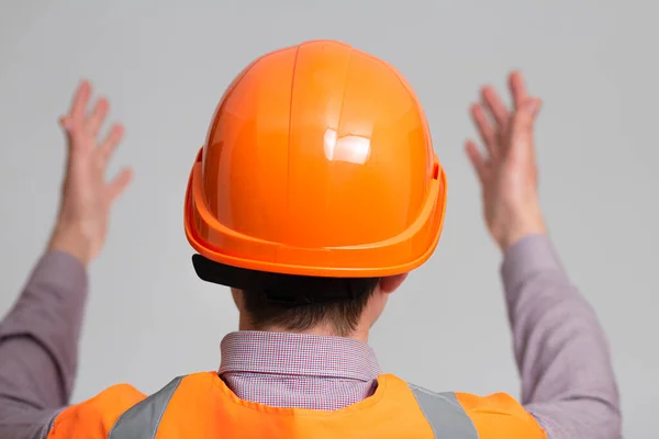 back of young contruction worker in hard hat spread his arms to the sides in confusion on grey studio background looking, foreman manage