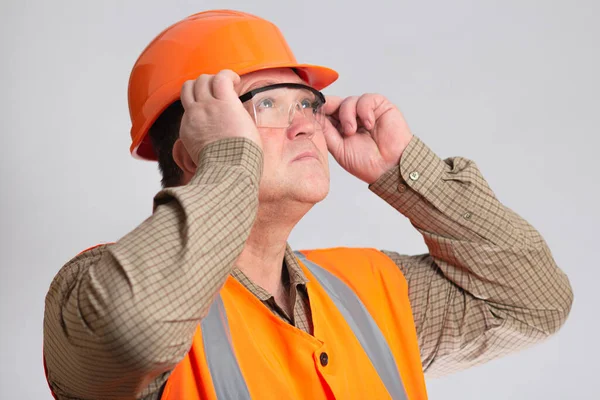 硬質帽子の中年の建築業者の顔は保護眼鏡をかけてグレーのスタジオの背景を見上げ — ストック写真