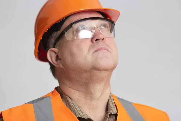 面对着自信的工程师 戴着橙色硬帽 戴着防护眼镜的中年建筑师 仰望着灰色工作室的背景 — 图库照片