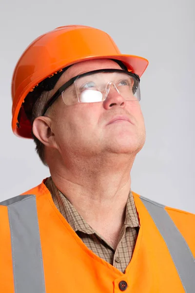 自信のあるエンジニア オレンジのハード帽子の中年建築家 グレーのスタジオの背景を見上げ保護眼鏡の顔 — ストック写真