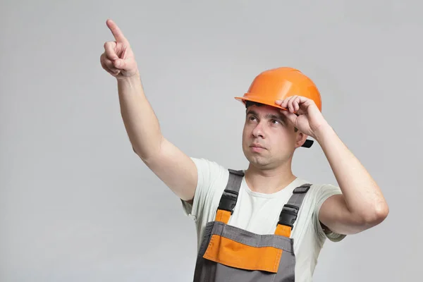 ハードハットの自信に満ちた若いフォアマンと全体の指を表示します 建設労働者はグレーのスタジオの背景に突きます ビル業界で広告 — ストック写真