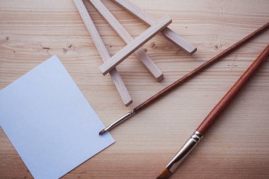 Doğanın önünde tahta minicik sehpada boş tuval ve boya fırçaları, sanat eserleri ve ilham konsepti, üst görünüm