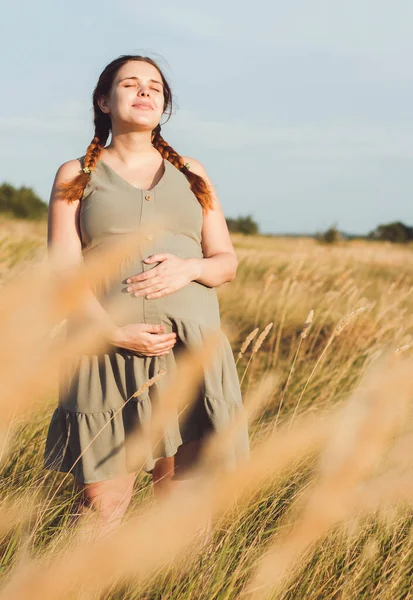年轻美丽的孕妇 红头发 日落时分 在干枯蓬松的草丛中 在田野里散步 在夏日的自然中 在为分娩做准备 在快乐健康的母亲 — 图库照片