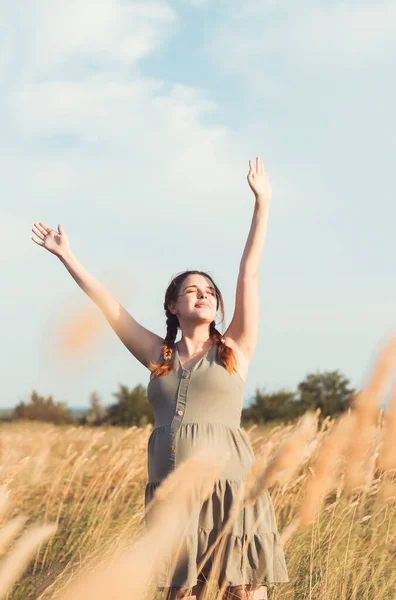 若い妊娠中の女性は夕暮れ時に乾いたふわふわの草の間を歩き夏の自然をリラックスし出産の準備と幸せ健康な母親として — ストック写真