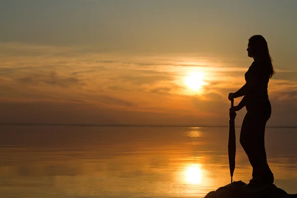 Silhouette di una ragazza con un ombrellone al tramonto sulla spiaggia — Foto Stock