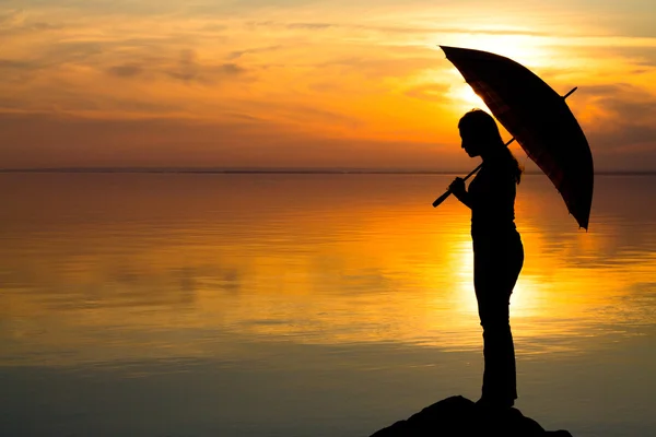 Silhouette di una ragazza con un ombrellone al tramonto sulla spiaggia — Foto Stock