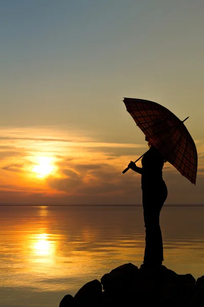 Silhouette di una ragazza con un ombrellone al tramonto sulla spiaggia — Foto Stock